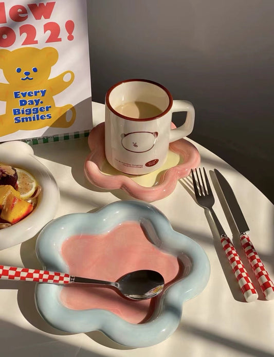 Cup with saucer, pink plate, and cutlery on a table with a book in the background