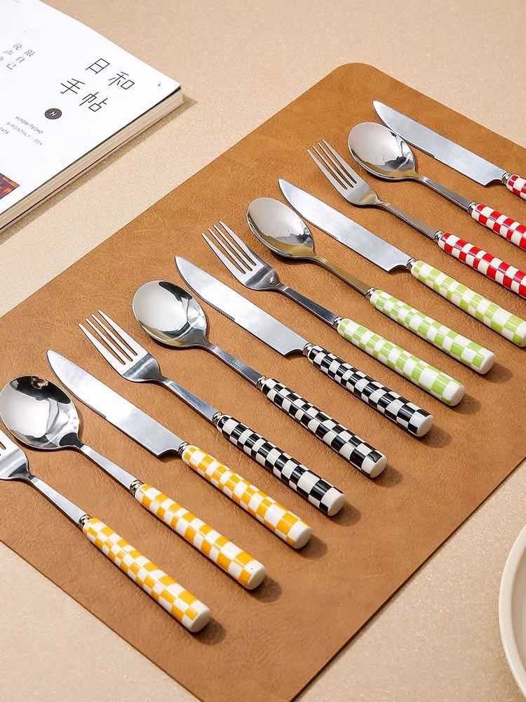 Set of silver cutlery with colorful handles on a brown placemat.