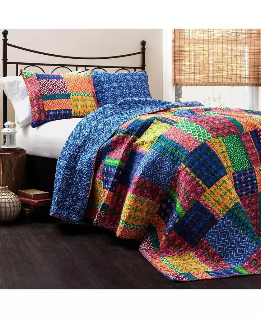 A colorful patchwork quilted bedding set on a bed, featuring a vibrant multicolor quilt and matching patterned pillow shams in blue, red, green, yellow, and orange, styled in a bedroom setting.