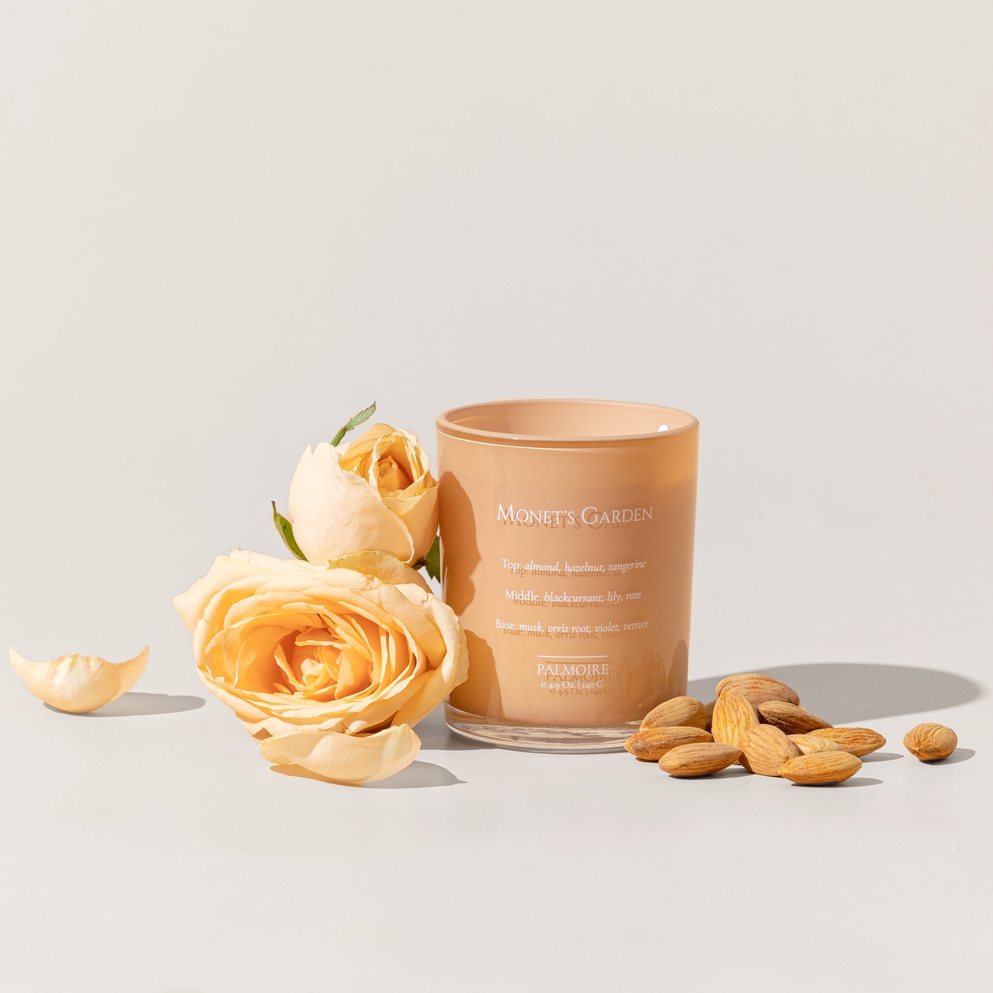 Candle labeled 'Monet's Garden' with almonds and roses on a light background