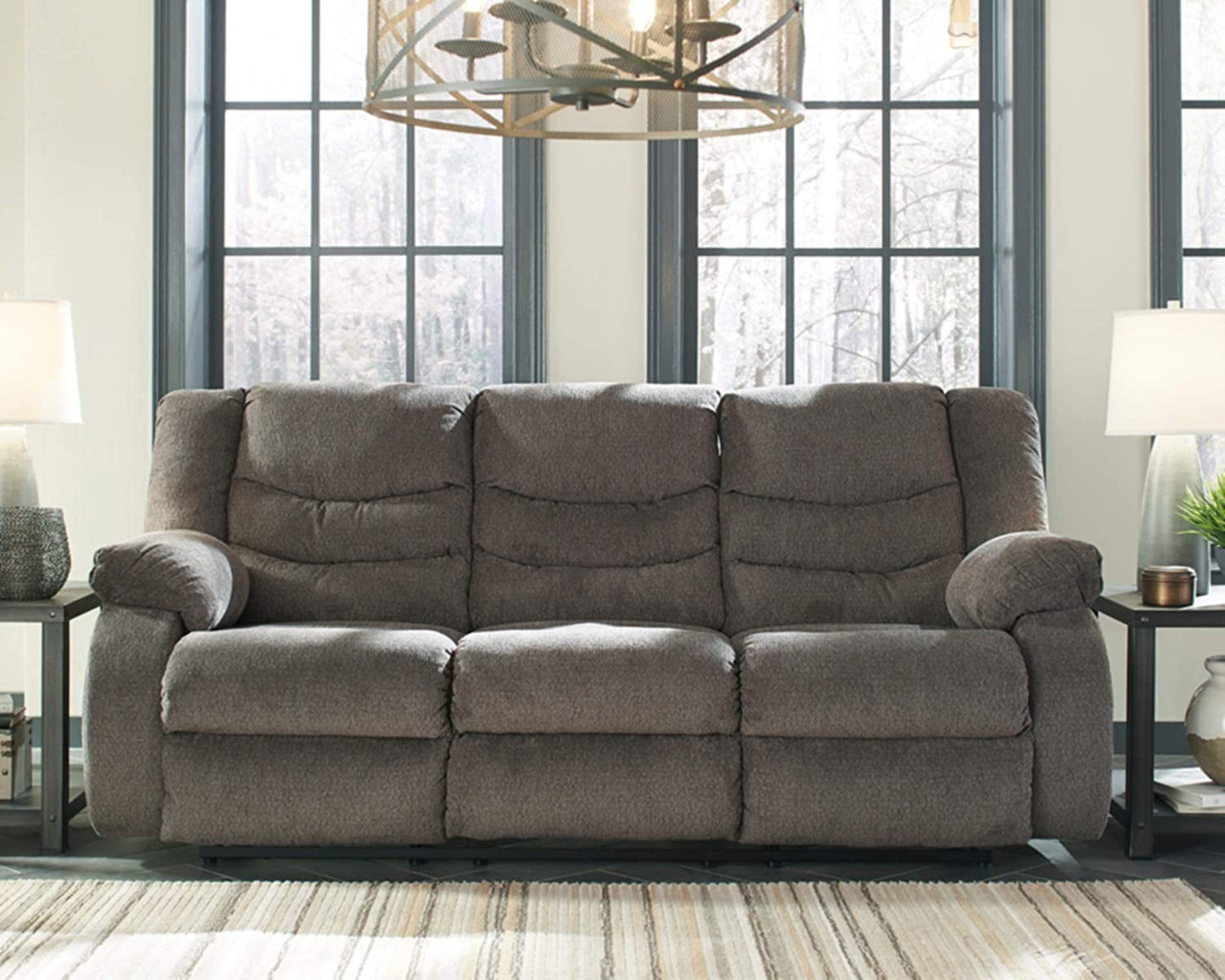Gray reclining sofa in a living room setting with large windows and decorative items.