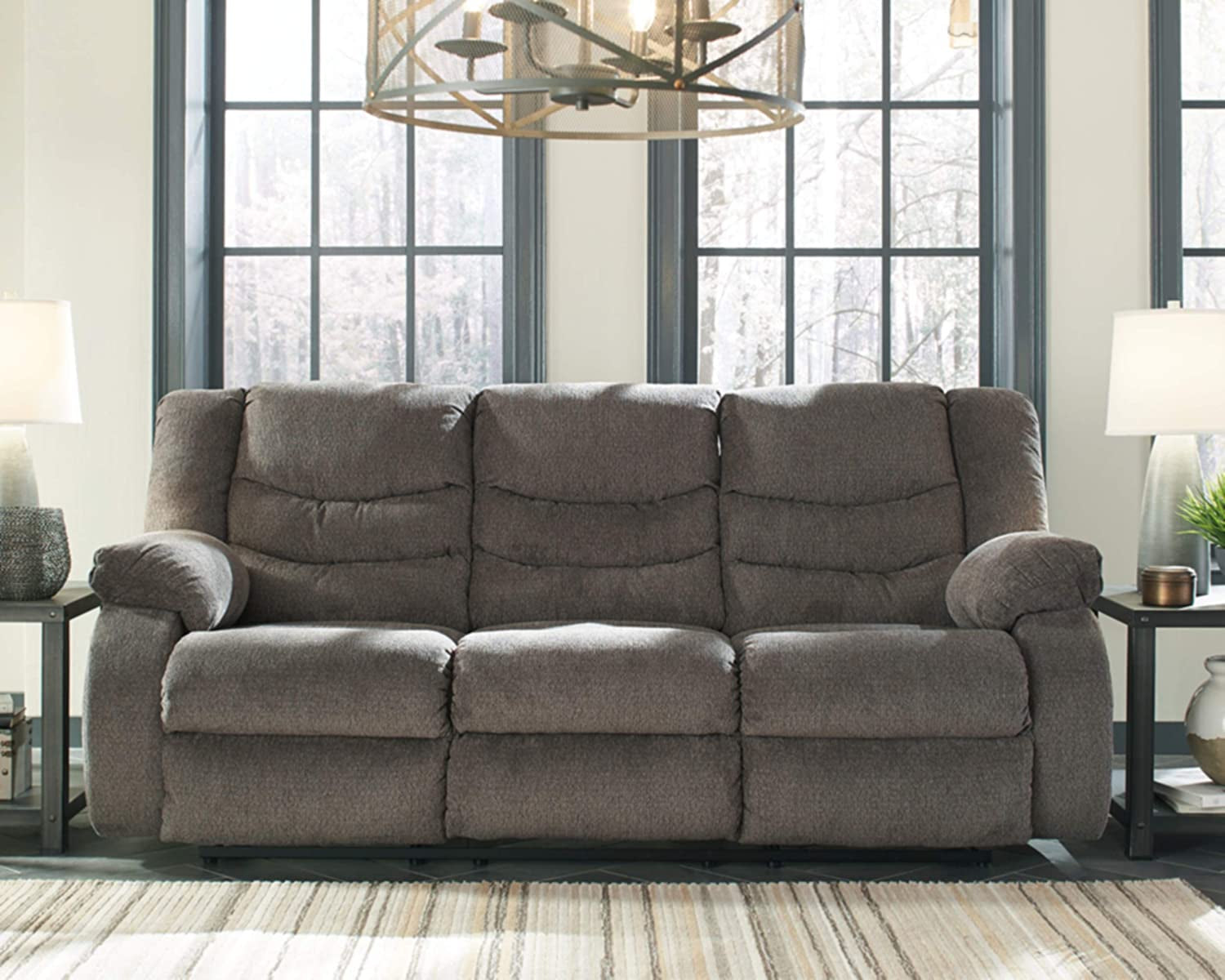 Gray reclining sofa in a living room setting with large windows and decorative items.