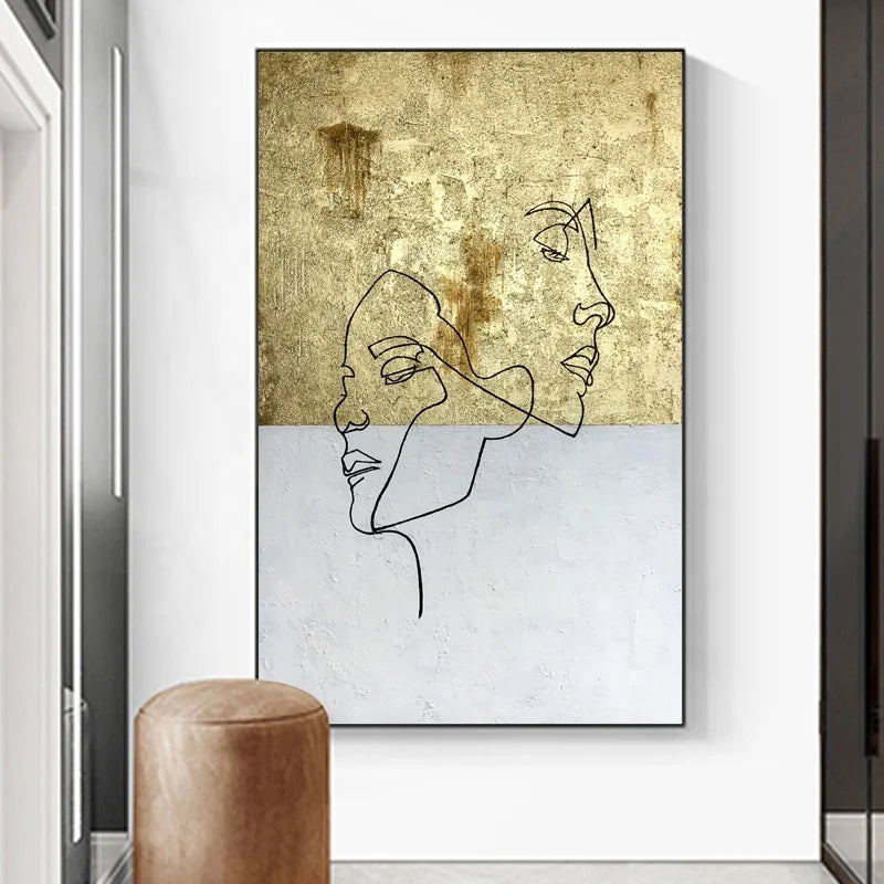 Framed abstract art with line drawings of faces on a textured gold and white background, displayed in a modern interior setting.