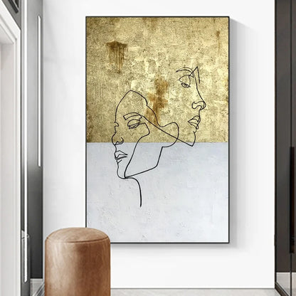 Framed abstract art with line drawings of faces on a textured gold and white background, displayed in a modern interior setting.