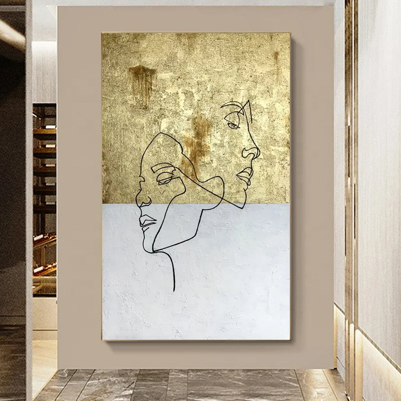 Abstract art piece with line drawings of faces on a textured gold and white background, framed in a modern interior setting.
