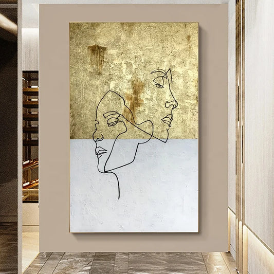 Abstract art piece with line drawings of faces on a textured gold and white background, framed in a modern interior setting.