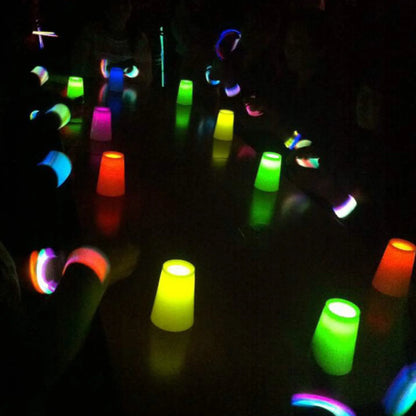A group of people glowing in the dark with colorful light-up plastic cups and wristbands on a black surface.