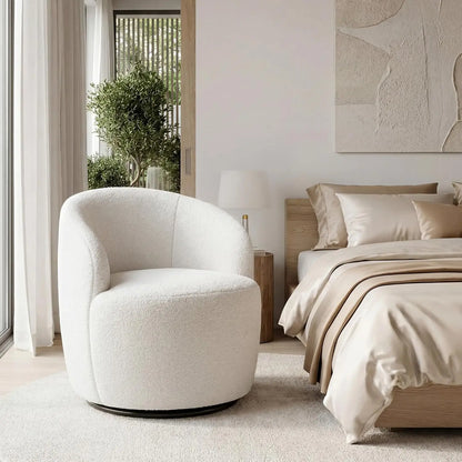 A modern round swivel armchair upholstered in textured boucle fabric, shown in a minimalist, neutral-toned bedroom setting next to a bed with beige bedding.
