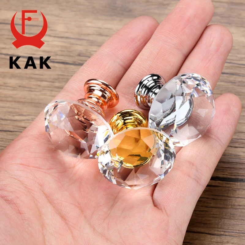 Clear crystal knobs with gold and rose gold finishes held in a hand, brand 'KAK' visible.