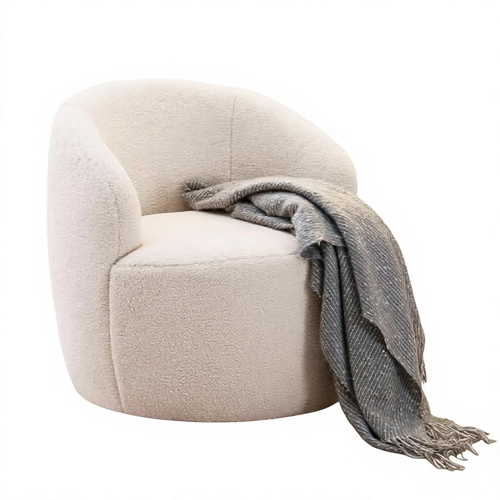 A modern round barrel chair upholstered in a textured cream bouclé fabric, styled with a gray woven throw blanket draped over the side, set against a plain white background.