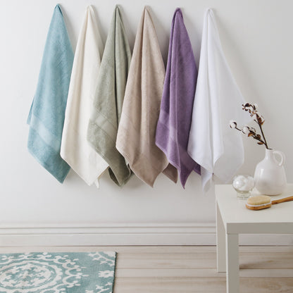 Five colorful towels hanging on a rack against a white wall with a small table and decorative items in the foreground.