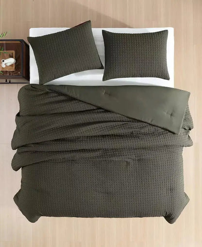 An overhead view of a bed dressed in an olive green textured waffle-weave bedding set, including a duvet cover and two matching pillowcases, set against a light wood-paneled background.