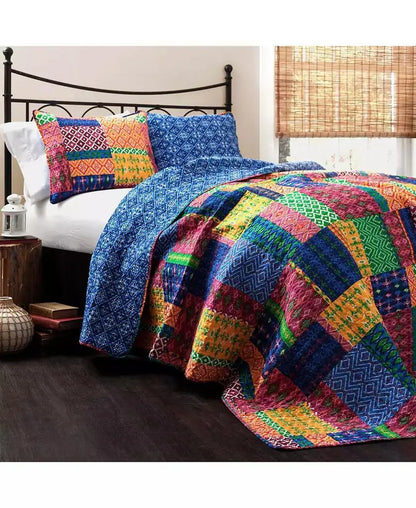 A colorful patchwork quilted bedding set on a bed, featuring a vibrant multicolor quilt and matching patterned pillow shams in blue, red, green, yellow, and orange, styled in a bedroom setting.