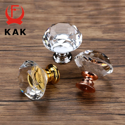 Clear crystal cabinet knobs with gold and bronze bases on a wooden surface, branded 'KAK'.
