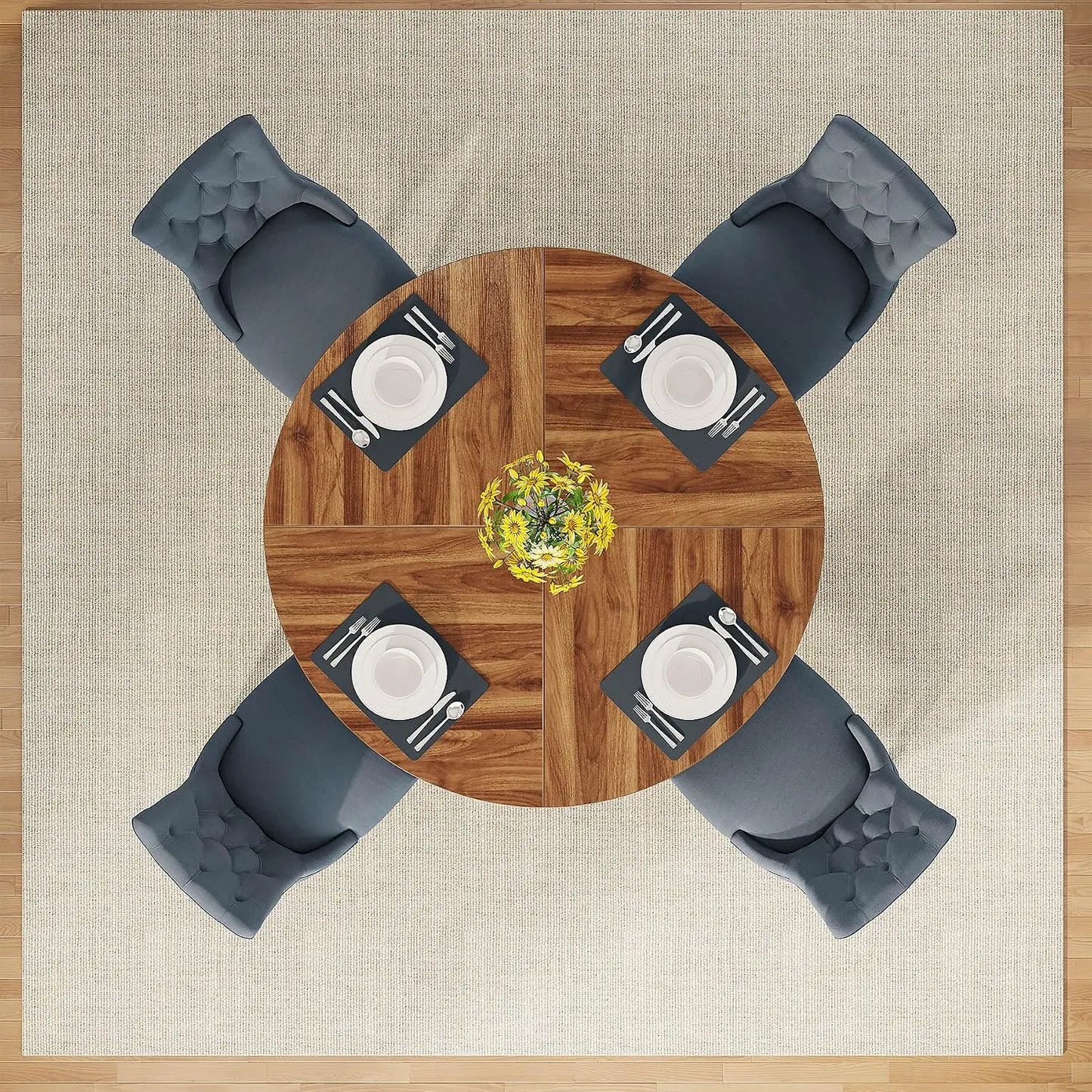 Overhead view of a round wooden dining table with four gray tufted chairs, set on a beige rug with a wood floor visible around the edges. Each chair is placed opposite the table, with white plates, black napkins, silver cutlery, and a small yellow floral centerpiece on the table.