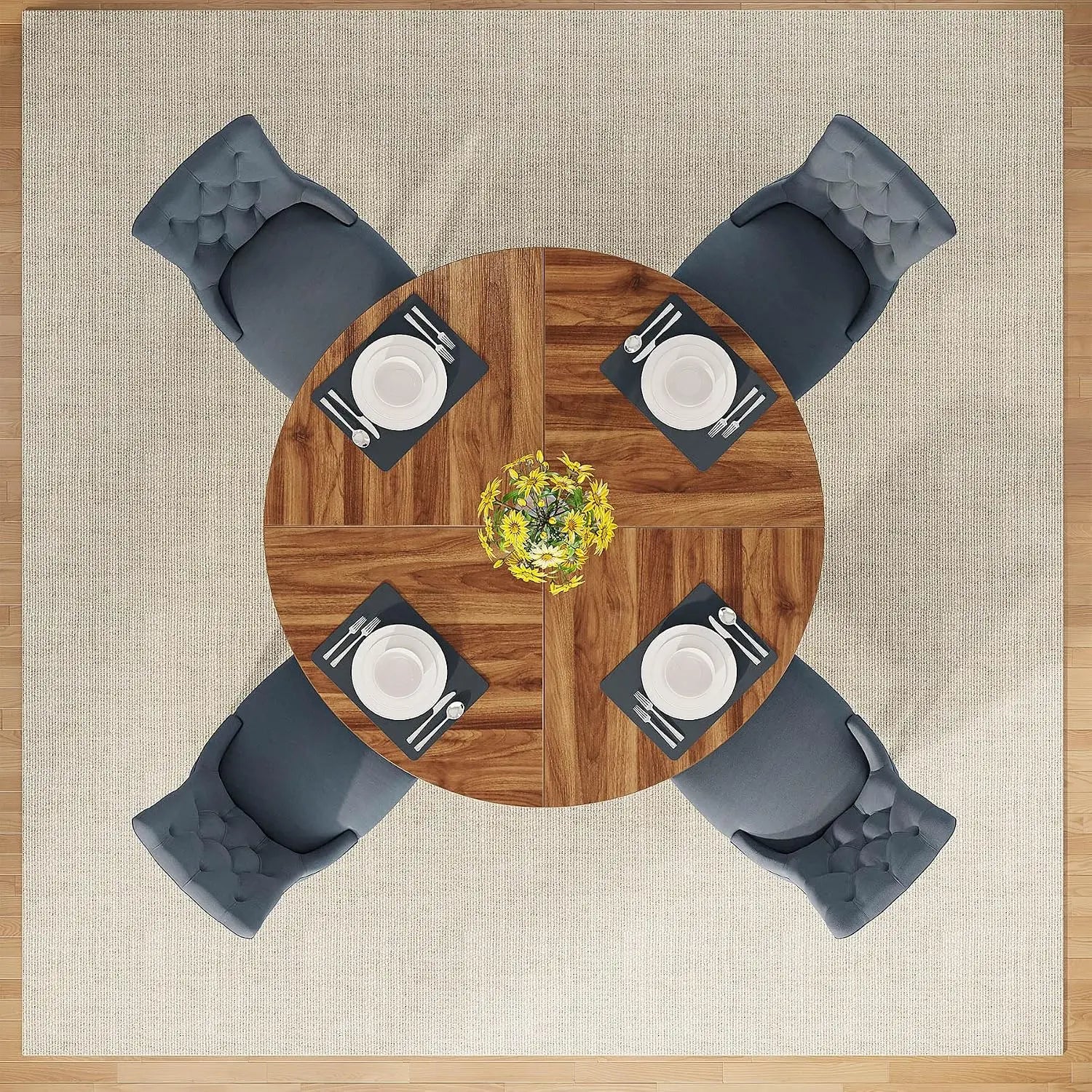 Overhead view of a round wooden dining table with four gray tufted chairs, set on a beige rug with a wood floor visible around the edges. Each chair is placed opposite the table, with white plates, black napkins, silver cutlery, and a small yellow floral centerpiece on the table.