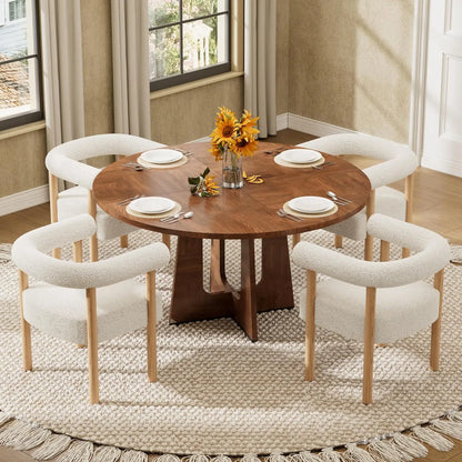 Round wooden dining table set with six cream boucle upholstered chairs, styled with white plates and a sunflower centerpiece in a bright dining room.
