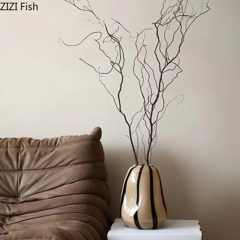 Decorative vase with branches on a white surface next to a brown cushion against a beige wall.