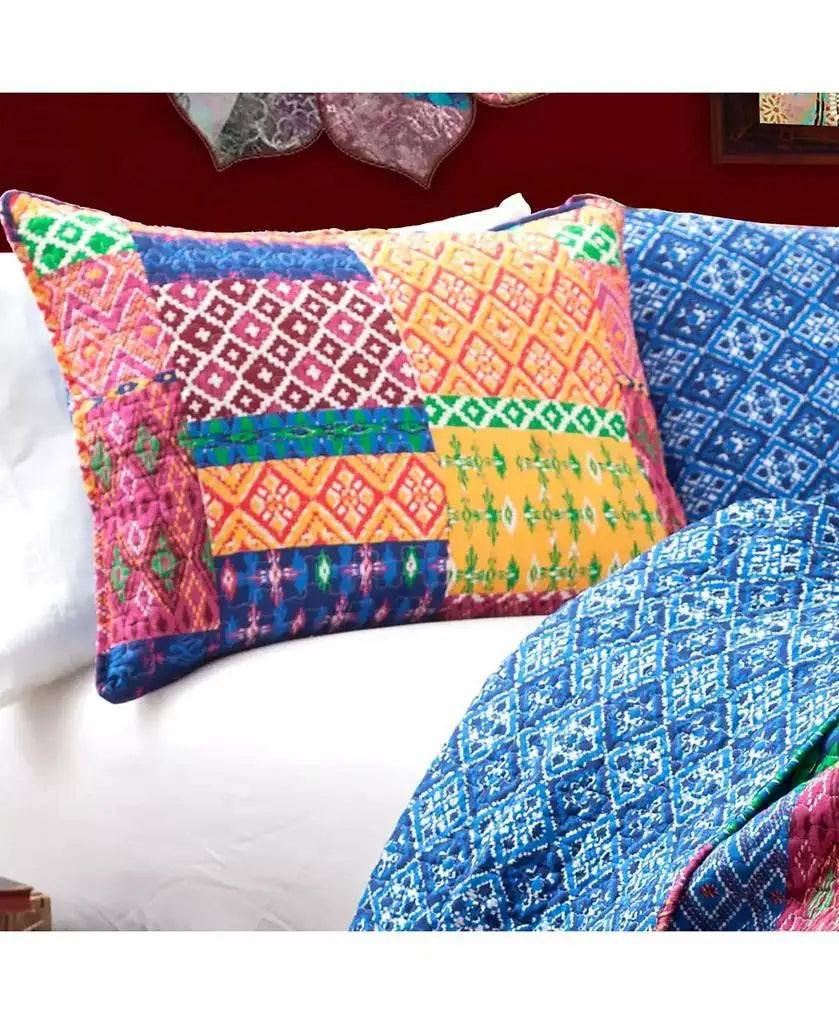 A colorful patchwork quilted pillowcase with vibrant geometric and ikat patterns in pink, orange, yellow, green, and blue, styled on a bed alongside a matching blue patterned quilt.