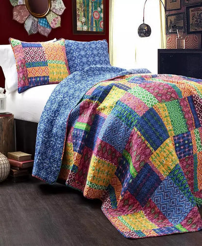 A colorful patchwork quilted bedding set on a bed in a styled bedroom, featuring a multicolor quilt with geometric patterns in blue, pink, yellow, green, and orange, along with matching patterned pillows.