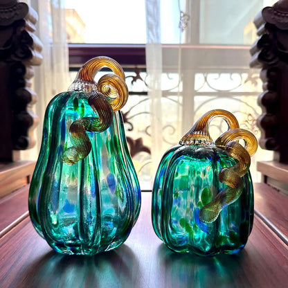 Two green glass pumpkins with gold accents on a reflective surface.