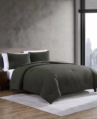 Modern bedroom with dark green textured duvet cover, matching pillows, warm wood furniture and city-view window.