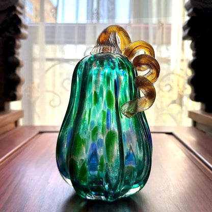Decorative glass pumpkin with green and amber colors on a wooden surface.