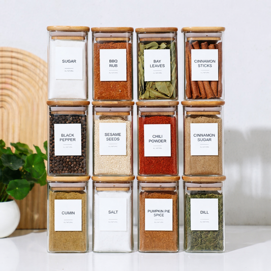 Collection of labeled spice jars on a white surface with a plant in the background.