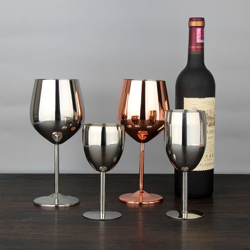 Four wine glasses of different colors and a bottle of wine on a wooden surface.