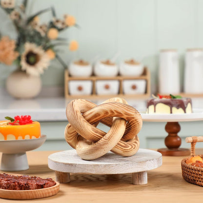 Wooden knot sculpture on a marble base with a blurred background of desserts and decor.