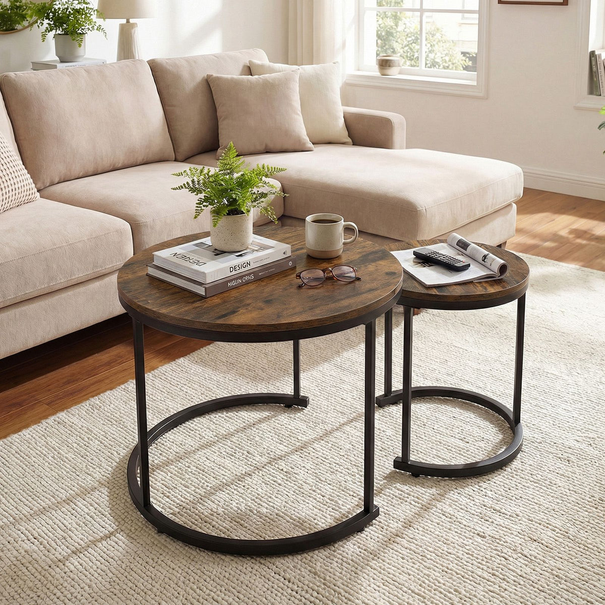 Two round nesting coffee tables with dark brown wood tops and black metal circular legs, styled in a bright living room next to a beige sectional sofa.