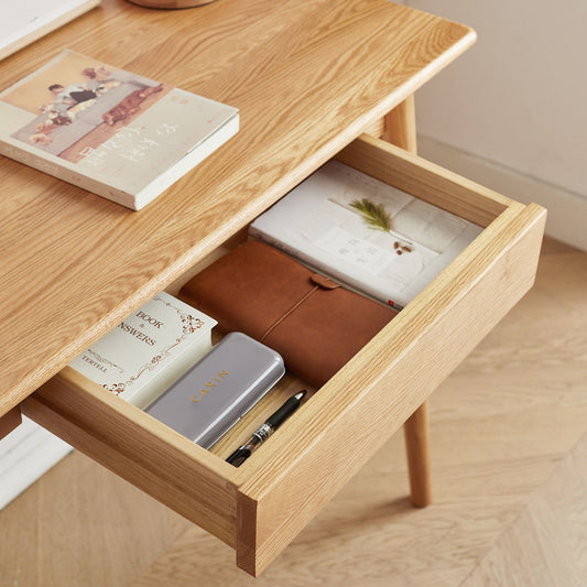 Wooden desk with open drawer containing stationery items on a wooden floor.