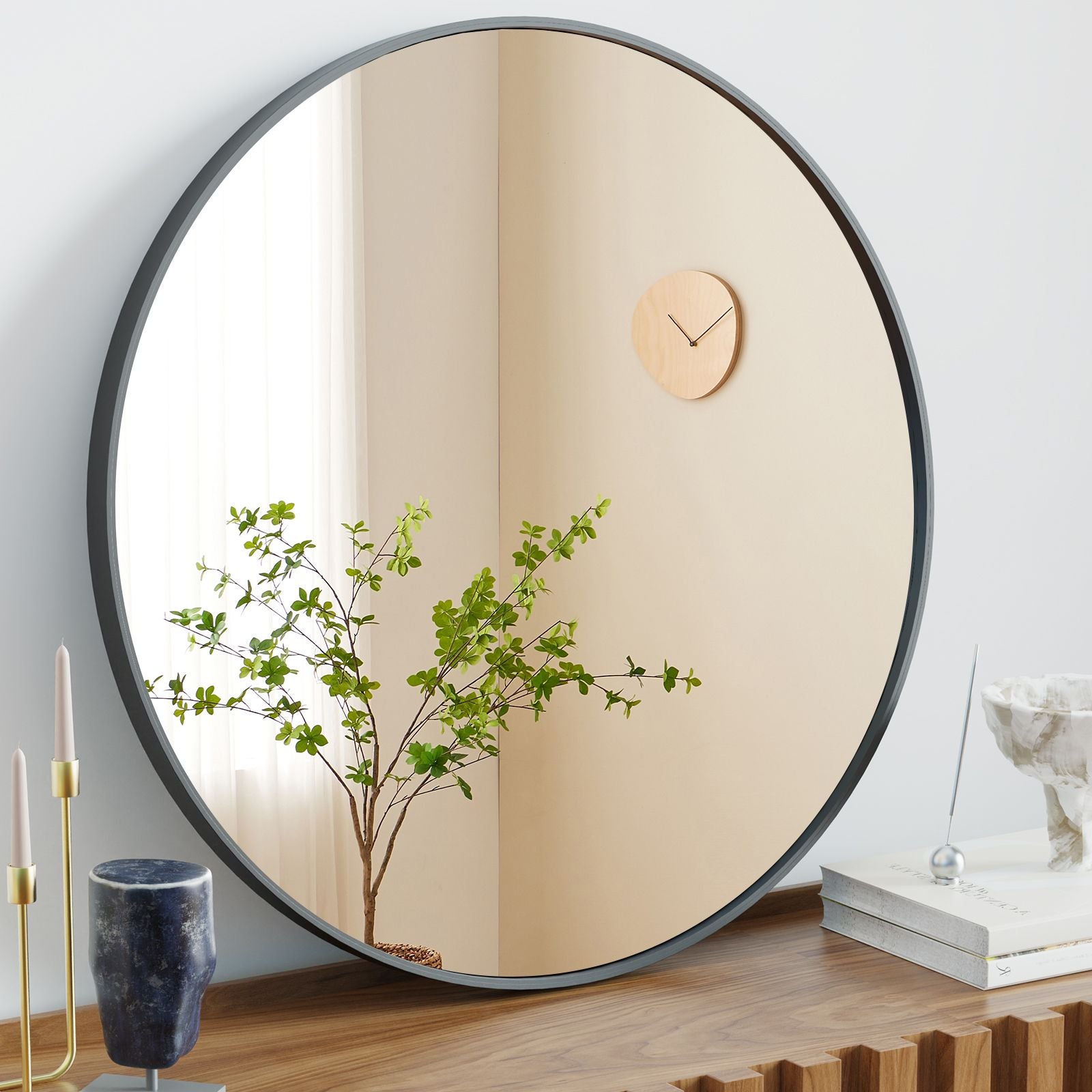 Round mirror with black frame reflecting a plant and clock on a wall.