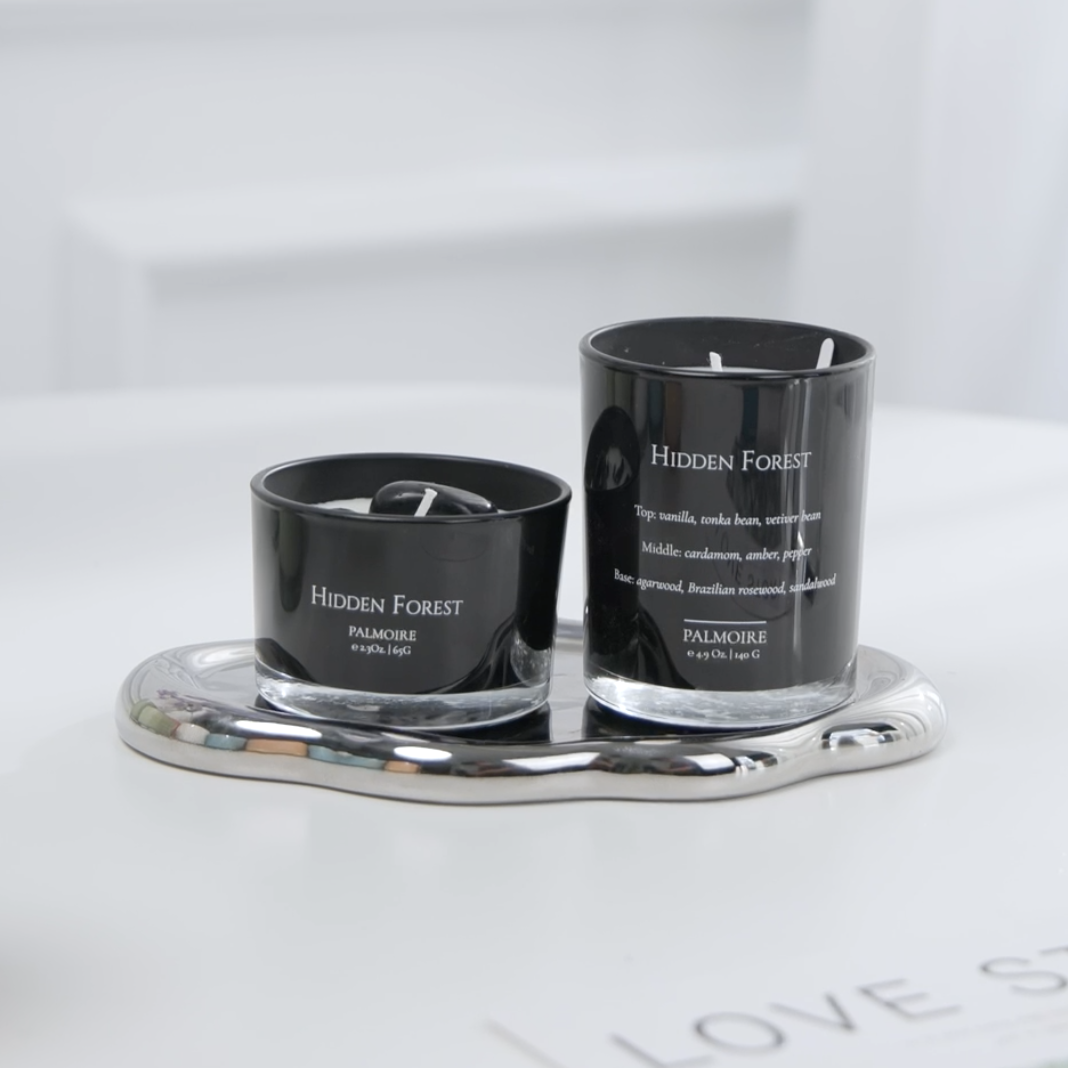 Two black candles labeled 'Hidden Forest' on a silver tray with a white background.