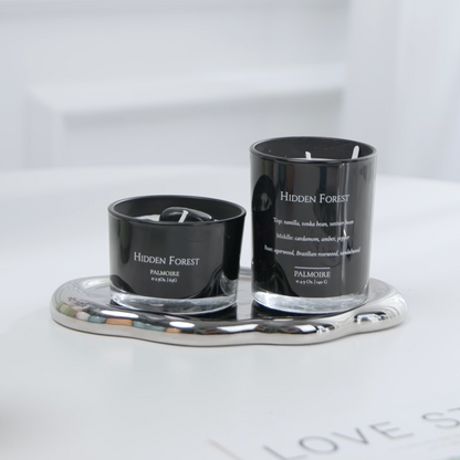Two black candles labeled 'Hidden Forest' on a silver tray with a white background.